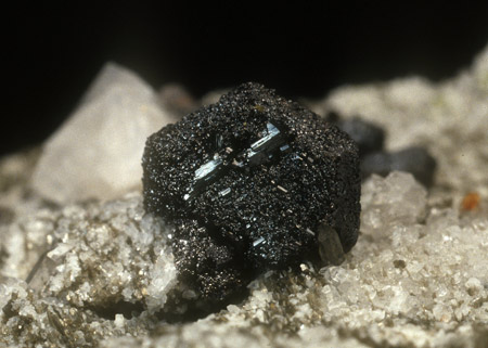 Pseudomorphose nach Ilmenit| (Durchmesser 14 mm), die oberflächlich aus Rutil mit sehr wenig Magnetit besteht und auf die ein winziger Anatas aufgewachsen ist 